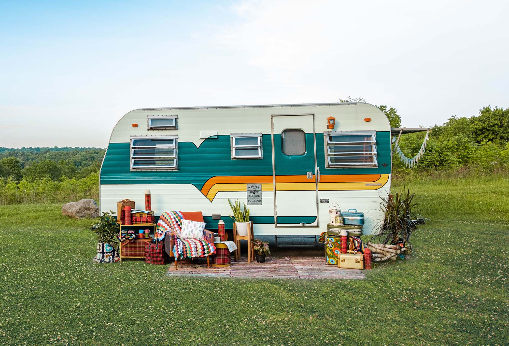 An older retro trailer surrounded by quaint country items.