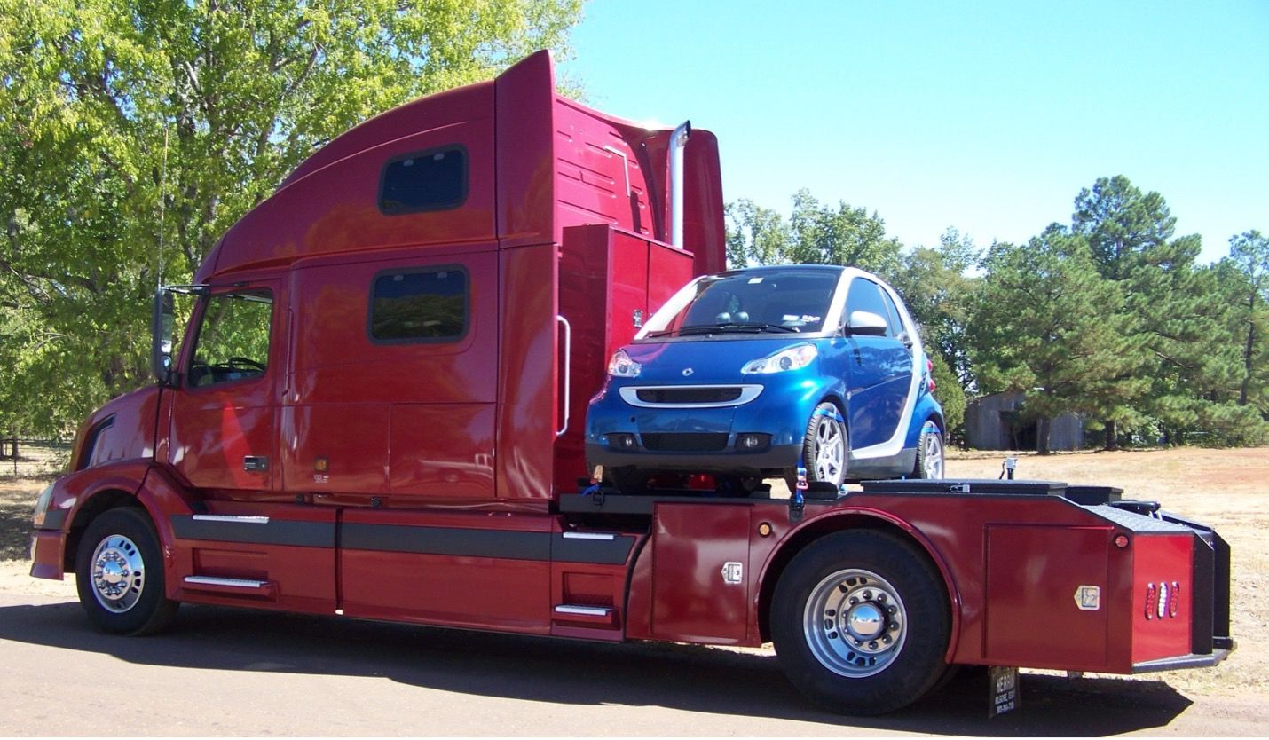 large red semi truck cab with smart car on bridge