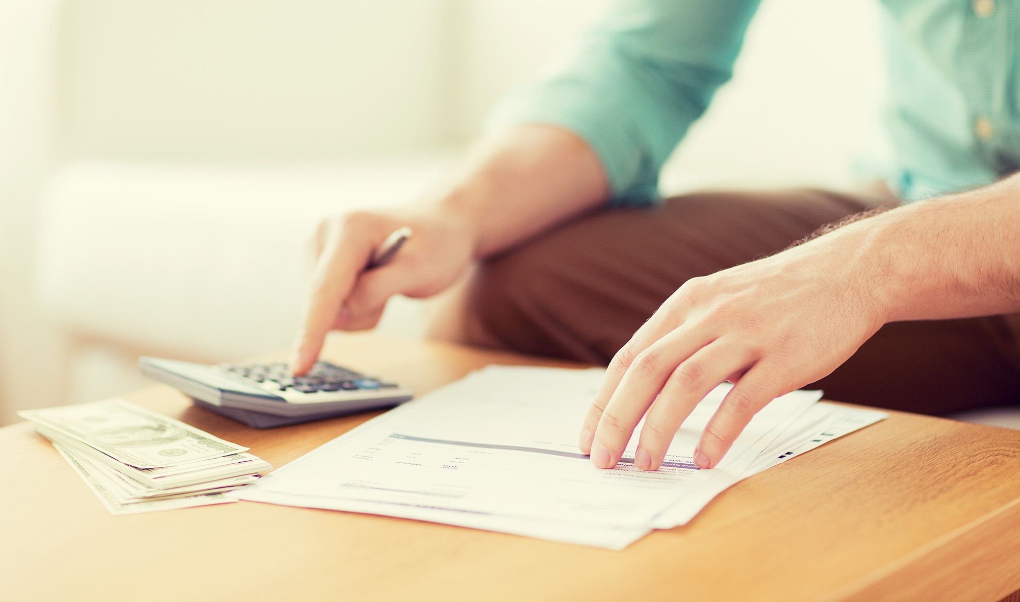 man sitting at a desk with calculator, cash and invoices.